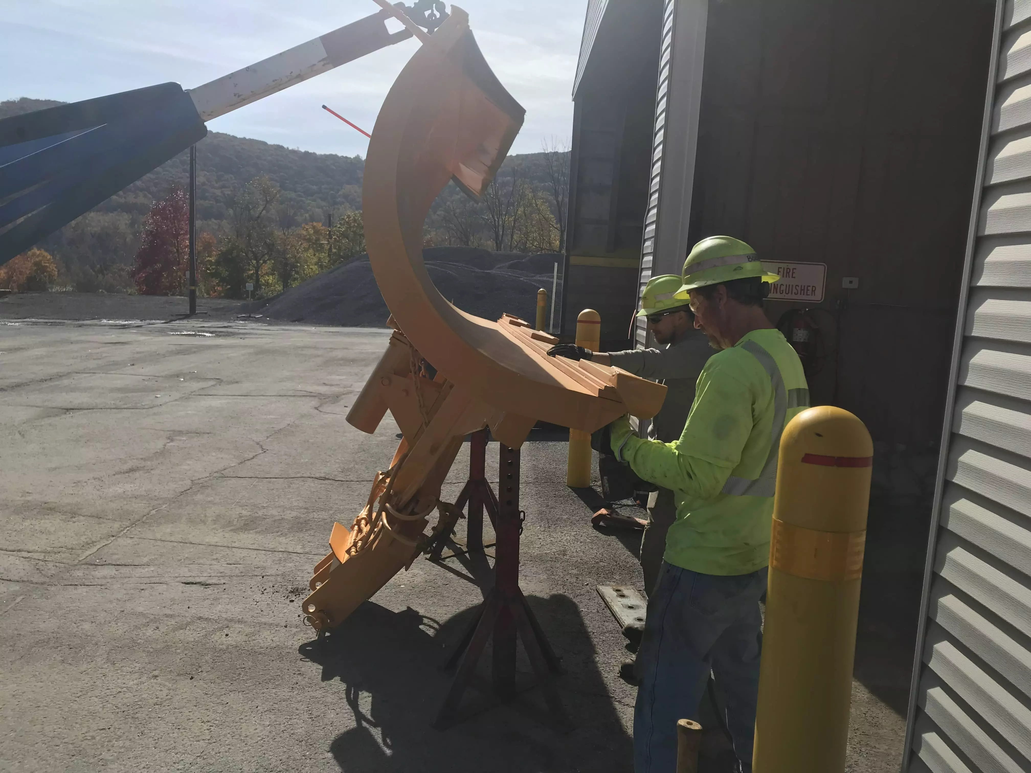Two PennDOT workers replace a snowplow blade at a PennDOT stockpile.